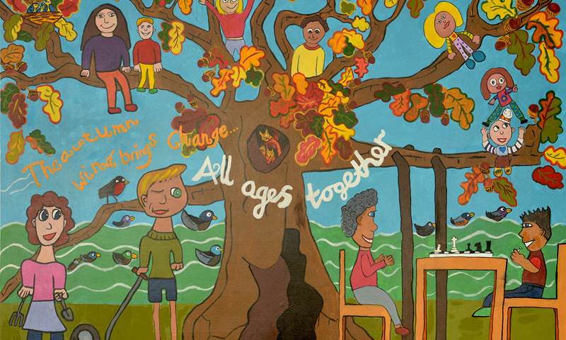 Painted mural of a tree with children climbing the branches and an adult and child playing chess underneath. The words "All ages together" are painted in white across the tree trunk.